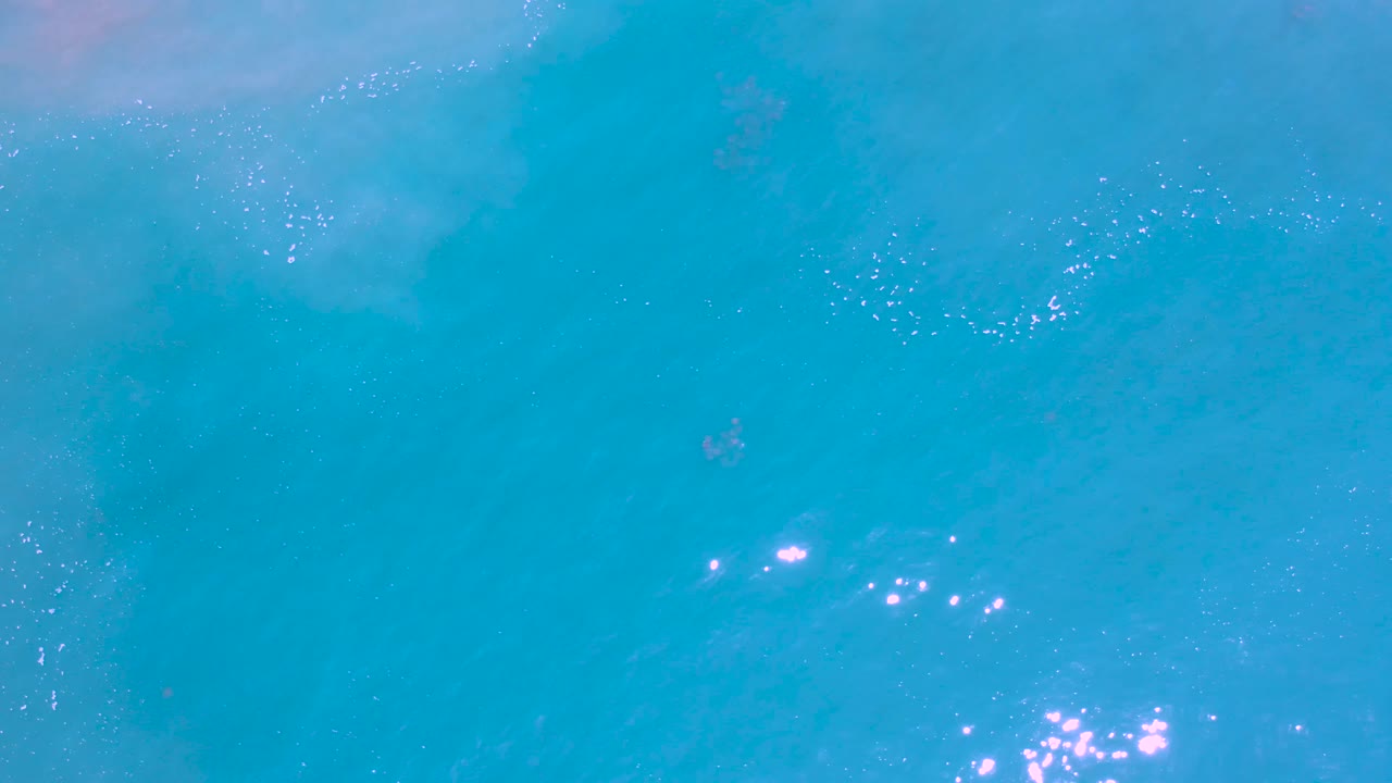 Turquoise Los Cabos ocean surface with brighter reflective points near the lower center and no visible people.