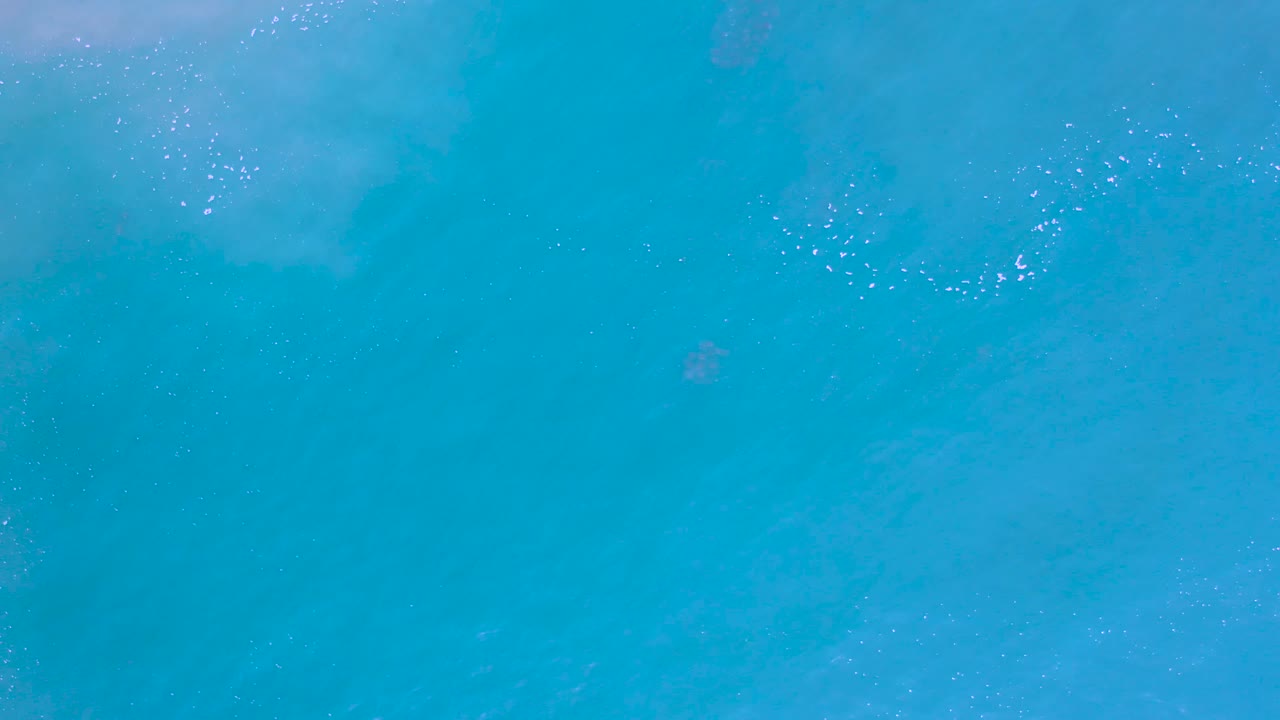 Overhead view of turquoise ocean water in Los Cabos, Mexico with faint foam near the upper edge and no visible people.