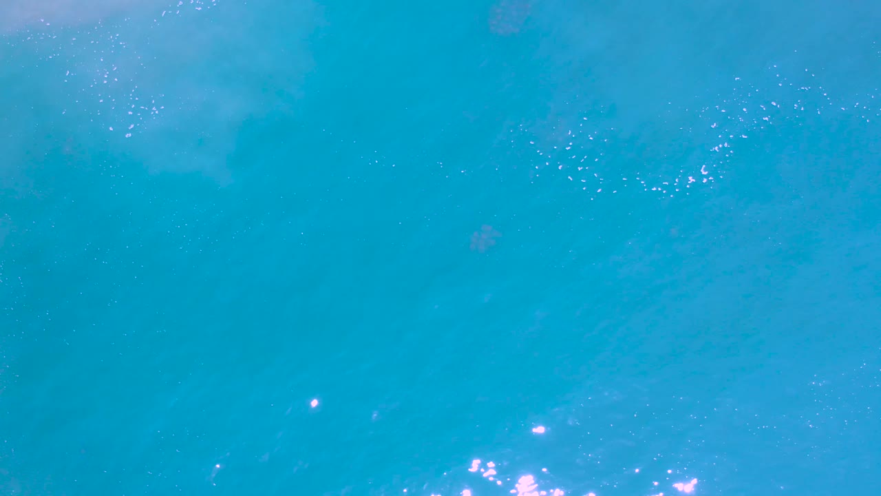 Turquoise ocean water in Los Cabos, Mexico fills the frame, with scattered bright glints along the lower right and no visible people.