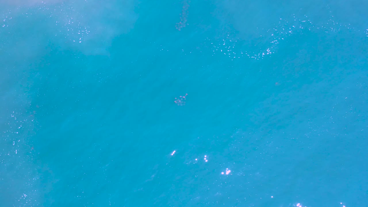 Top-down Los Cabos water view with open turquoise color, soft pale underwater shapes, small sparkle points, and no visible people.