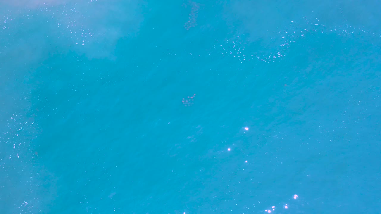 Turquoise sea with a darker small patch and soft surface shimmer.