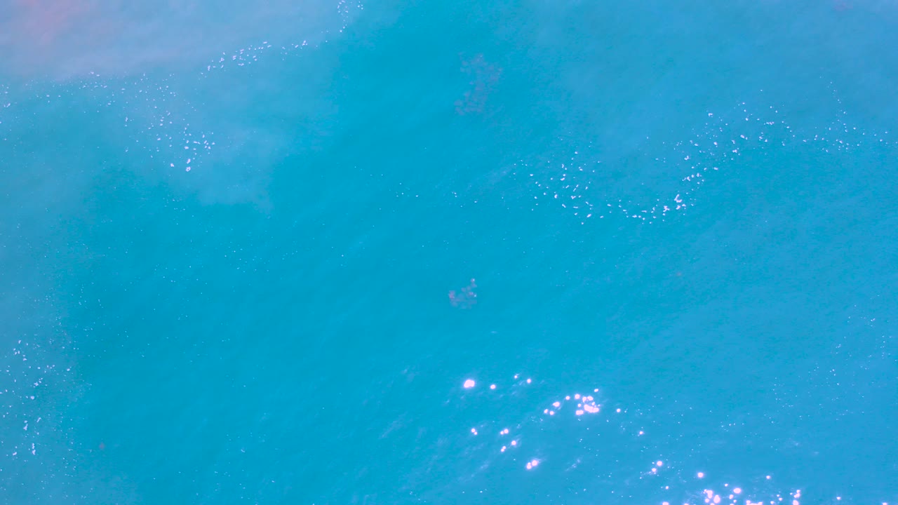 Overhead view of turquoise ocean water in Los Cabos, Mexico, with scattered sun sparkles and no visible people.