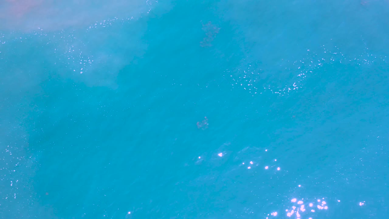 Open turquoise sea in Los Cabos, Mexico, filled by rippled water and a cluster of surface shimmer near the lower edge, with no visible people.