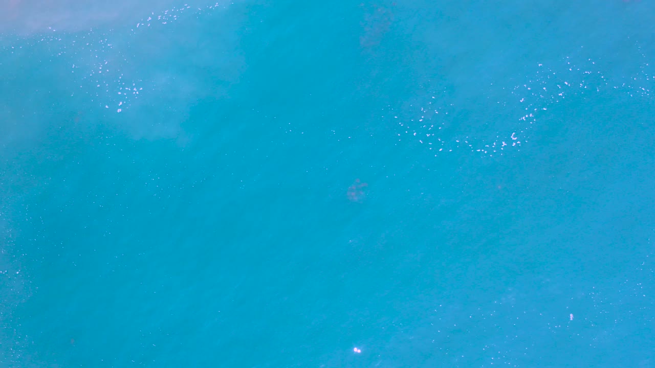Top-down aerial view of blue ocean water in Los Cabos, Mexico, with faint foam near the upper edge and no visible people.