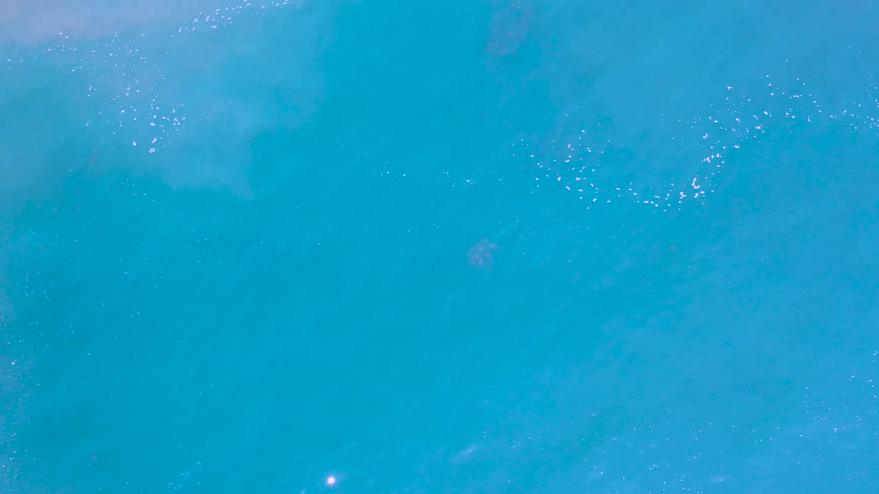 Blue water viewed from above with a brighter foam patch.