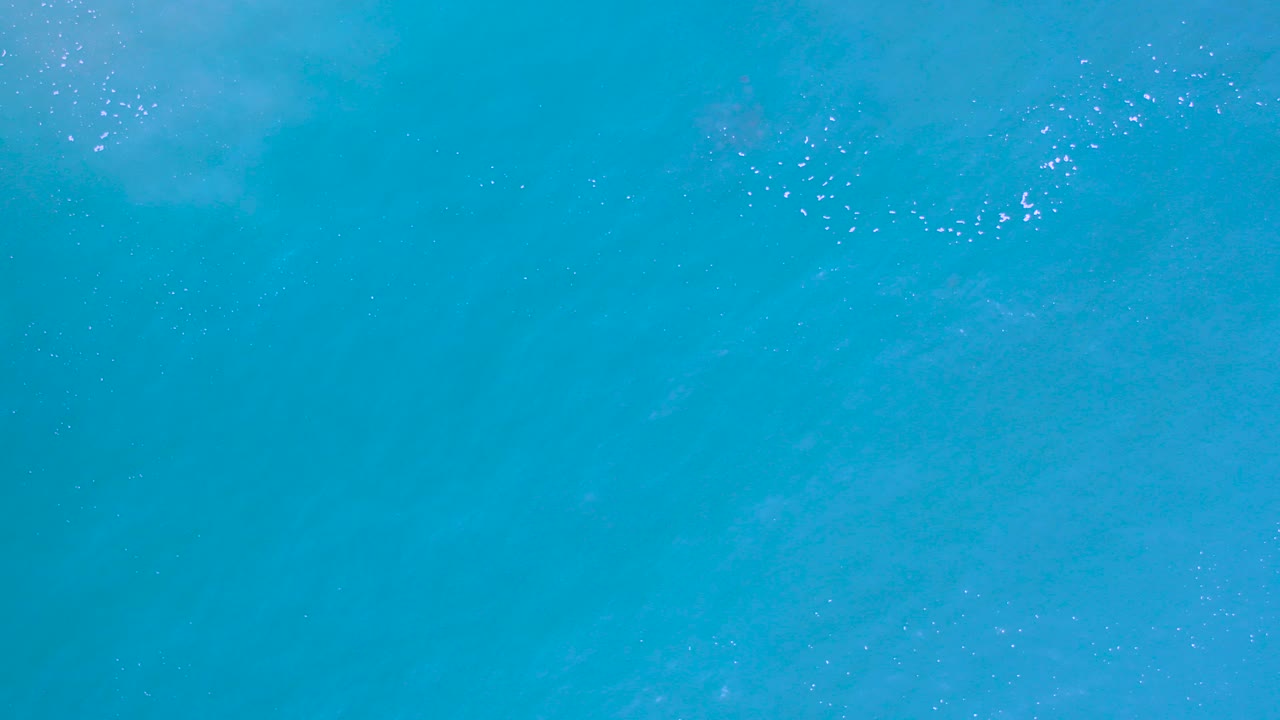 Overhead view of turquoise ocean water in Los Cabos, Mexico, with faint white foam near the upper area and no visible people.