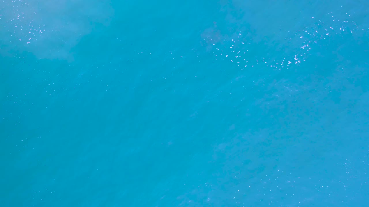 Overhead Los Cabos water frame with blue-green color, scattered tiny highlights, soft underwater texture, and no visible people.