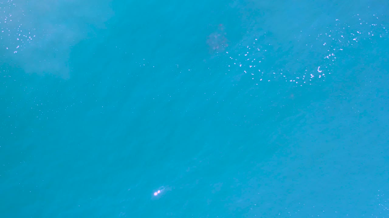 Overhead ocean water with a loose cluster of white foam specks.