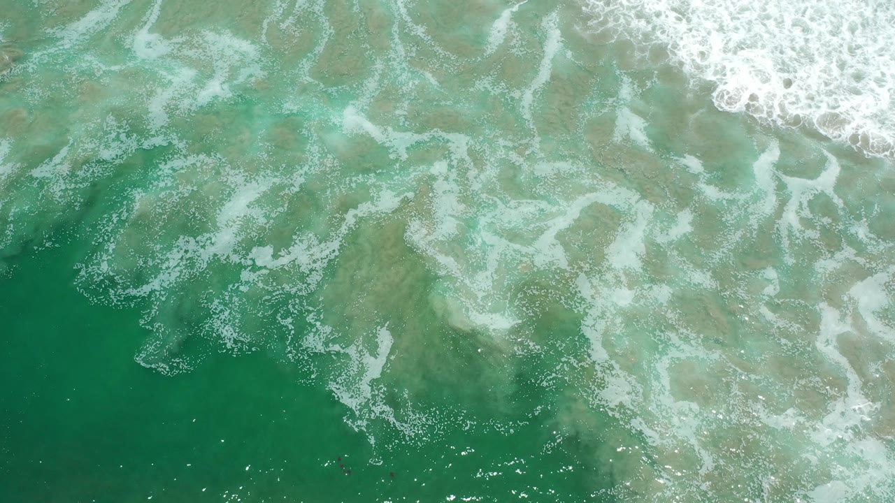 Emerald water with pale foam and sandy shallows below.
