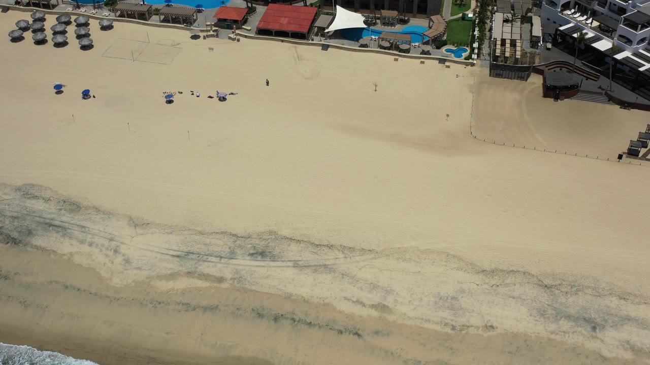 Overhead beach resort with pools, cabanas, umbrellas, and shoreline wash.