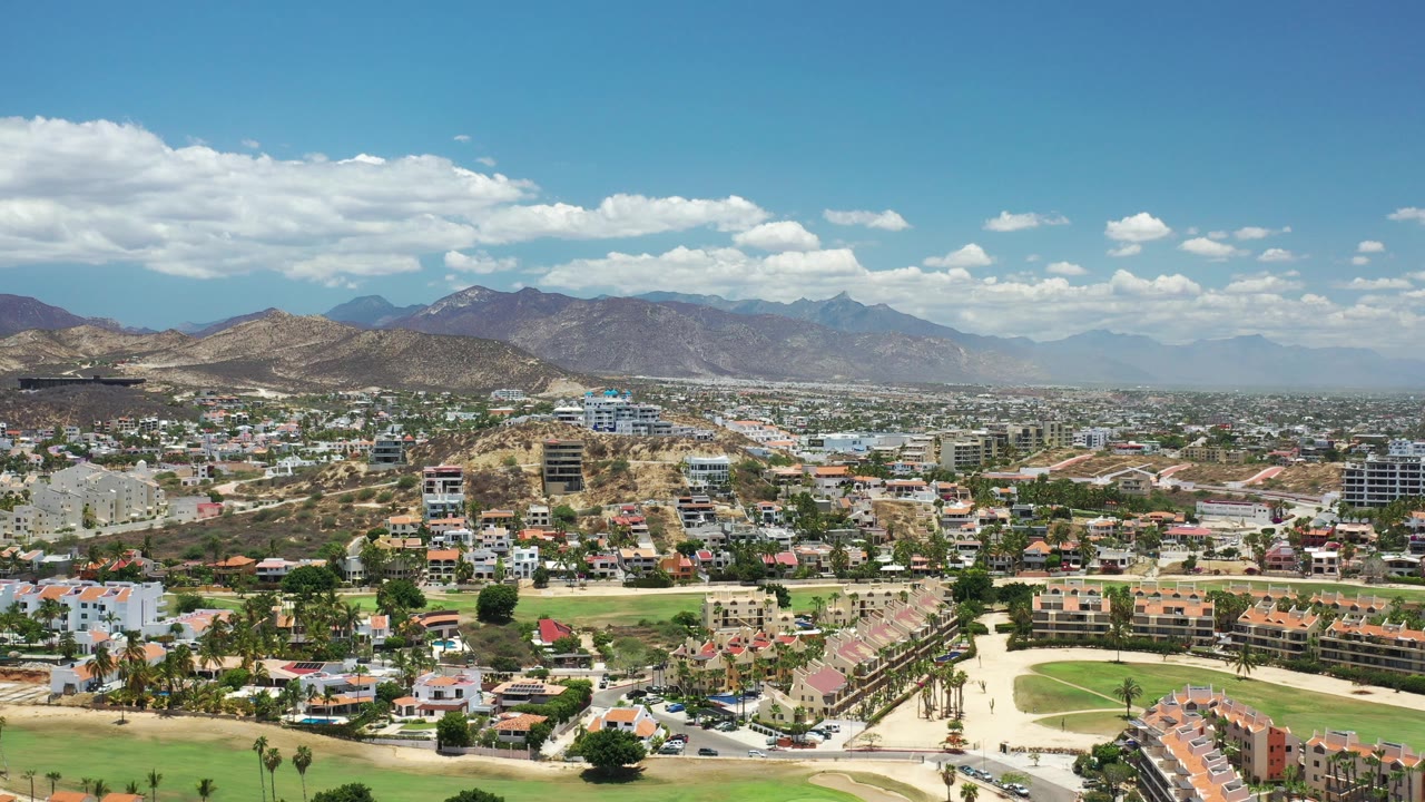 Aerial view of a Los Cabos city area with green fairways and mountains beyond.