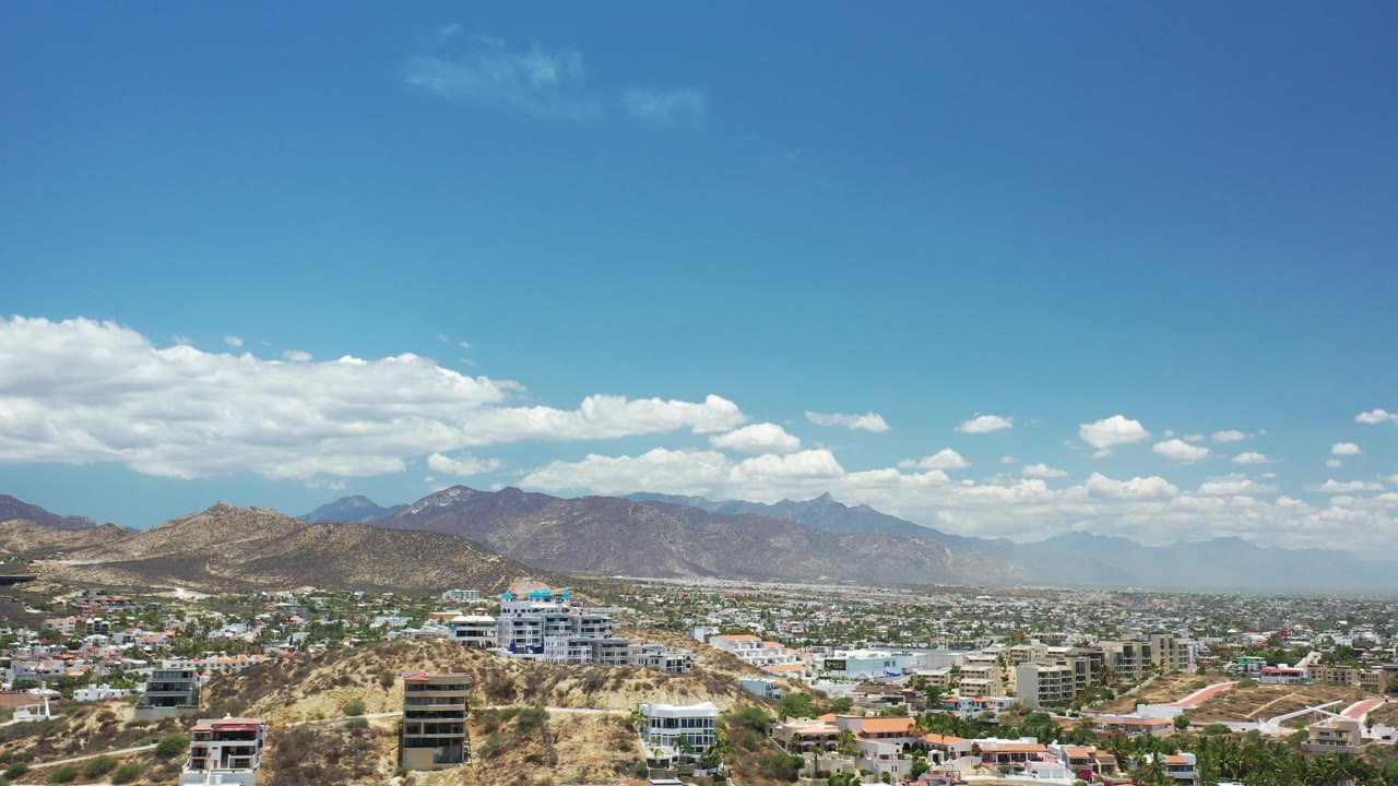 Elevated Los Cabos view with foreground homes, winding roads, hills, and mountains