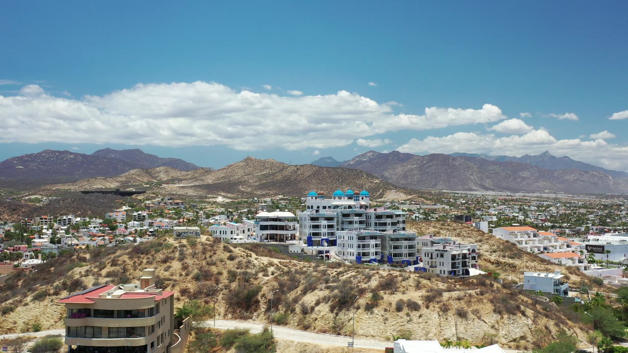 Aerial view of hillside buildings and desert mountains under blue sky.