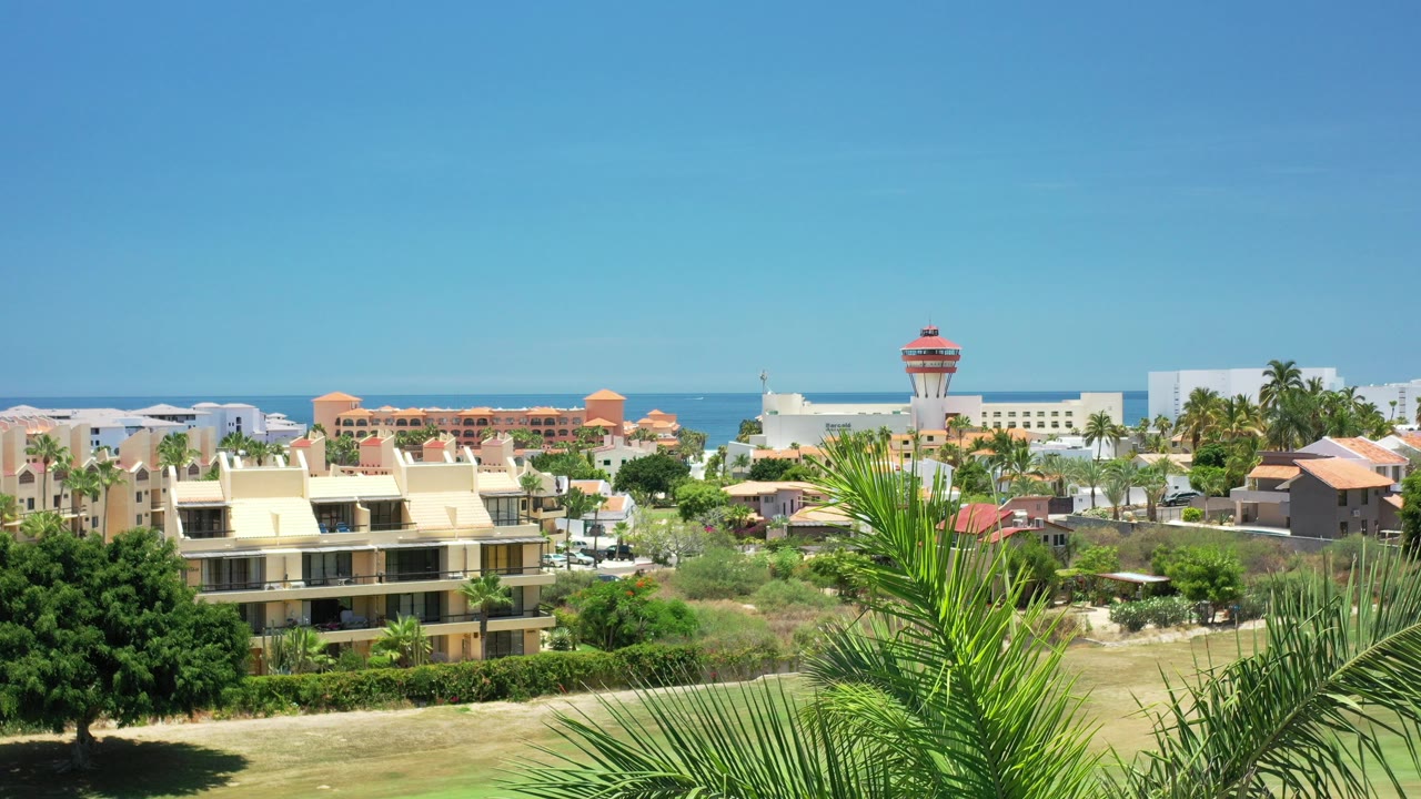 Elevated view of resort buildings, palms, trees, ocean, and blue sky.