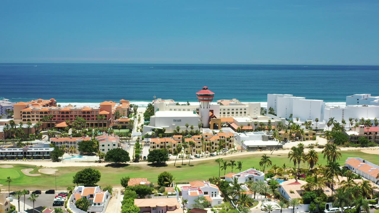 Coastal town with white buildings, orange roofs, palms, and ocean