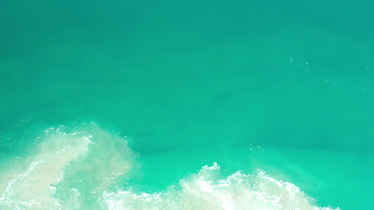 Aqua ocean surface with pale foam along the lower left and bottom.