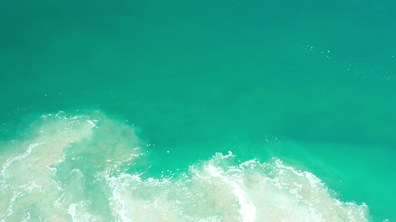 Top-down Los Cabos ocean frame with blue-green water, pale foam across the lower third, and no visible people or boats.