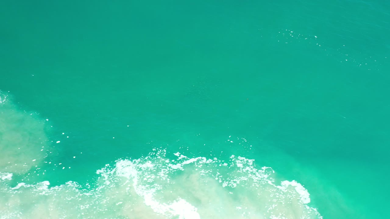 Turquoise sea surface in Los Cabos, Mexico, with white foamy surf entering from the lower edge and no visible people.