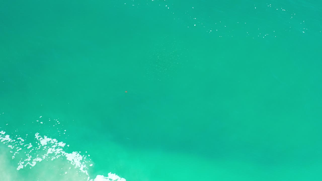 Overhead view of turquoise ocean in Los Cabos, Mexico, with white foam entering from the lower left and no visible people.