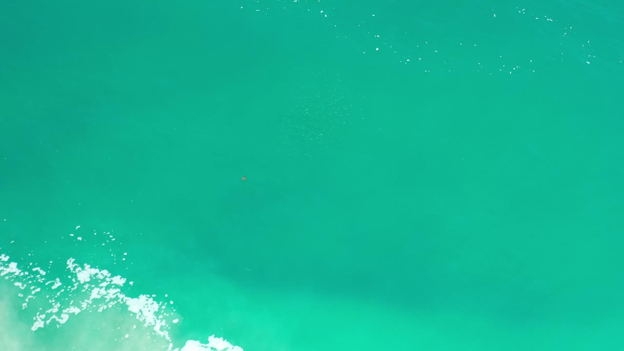 Bird's-eye ocean view in Los Cabos, Mexico, with a compact white foam patch near the lower left and no visible people.