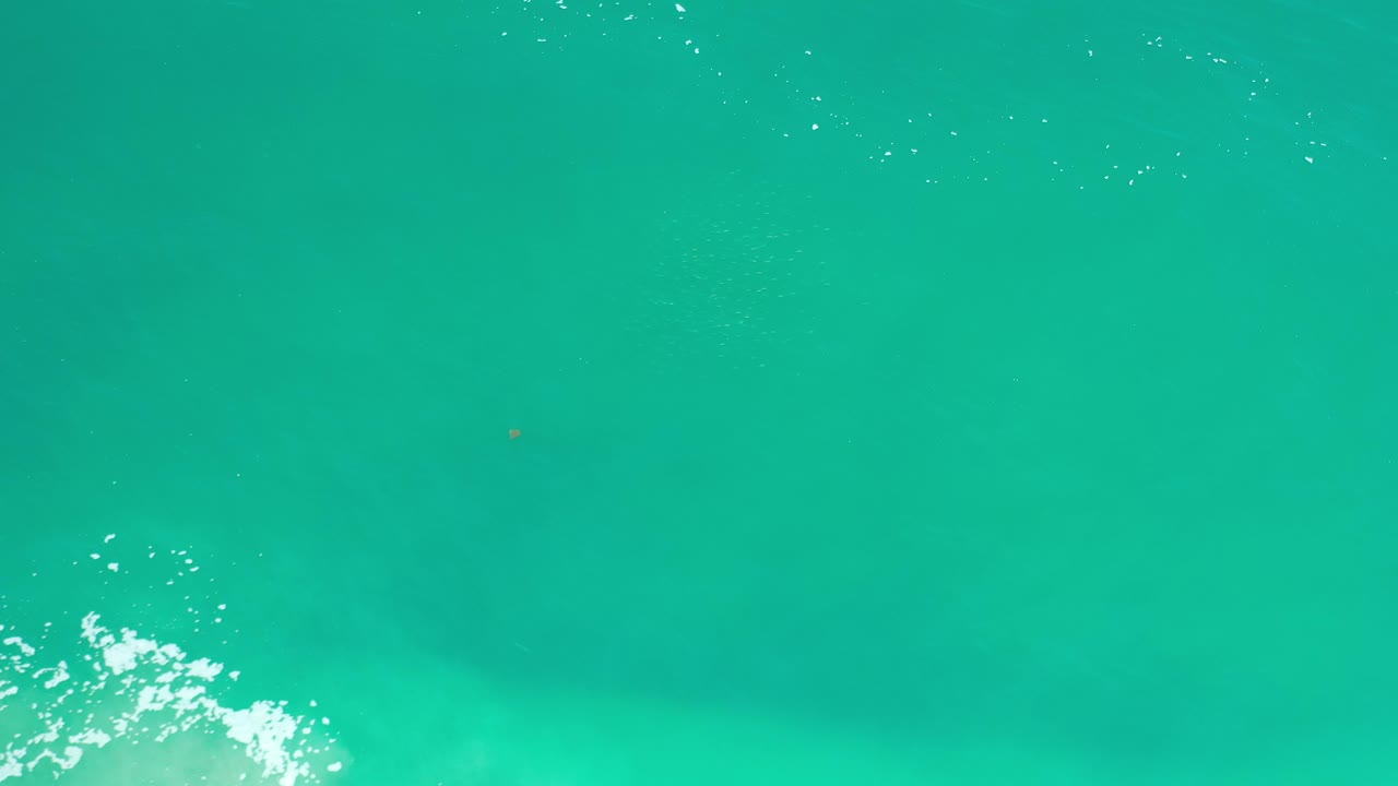 Aerial turquoise water with bright foam and ripples along the lower left.