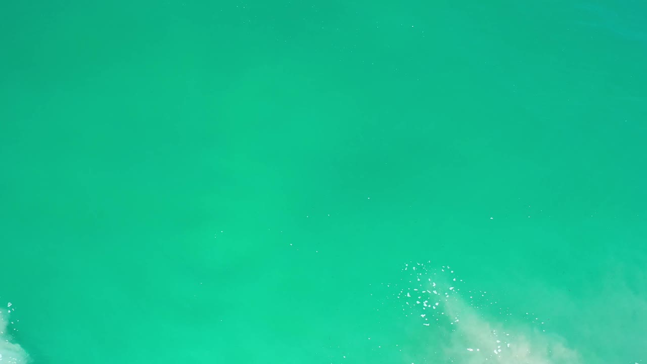 Clear green-blue ocean surface in Los Cabos, Mexico, with bright foam clustered near the lower left and no visible people.