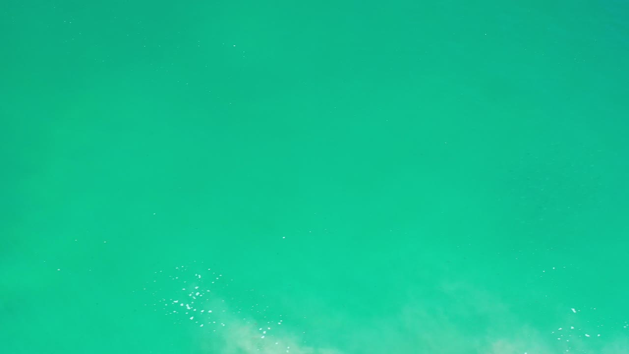 Teal ocean water in Los Cabos fills the frame with a faint band of pale foam entering near the lower left edge and no visible people.
