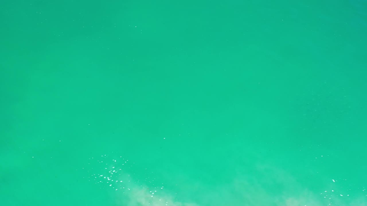 A closer patch of white foam spreads into the lower left of the teal Los Cabos water while the rest of the frame remains open water with no visible people.