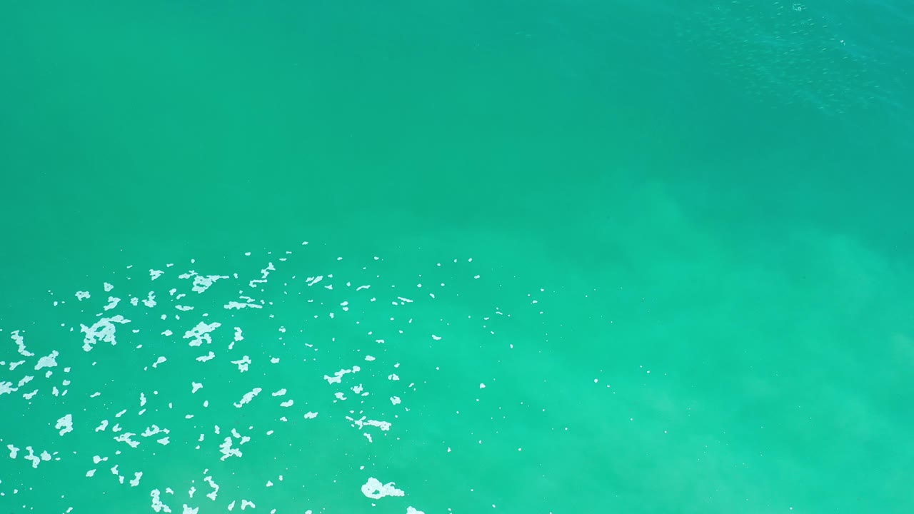 Turquoise sea surface with a small white foam patch at the lower left.