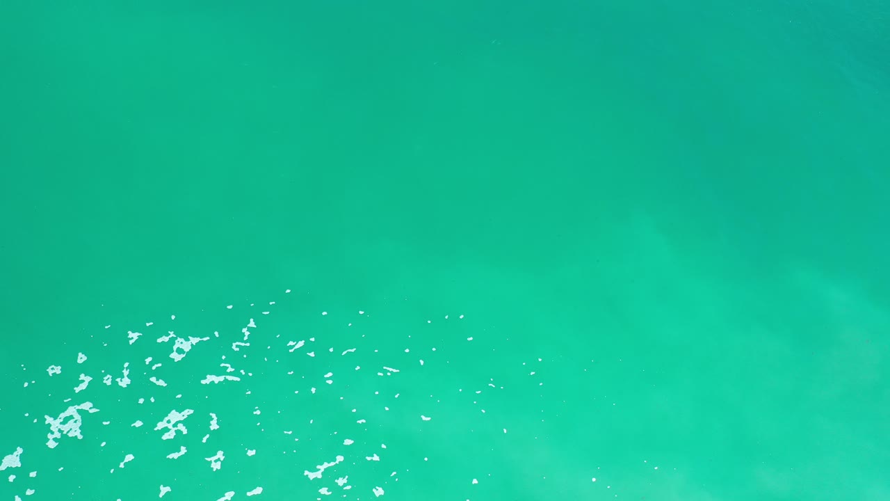 Top-down turquoise ocean with white foam flecks