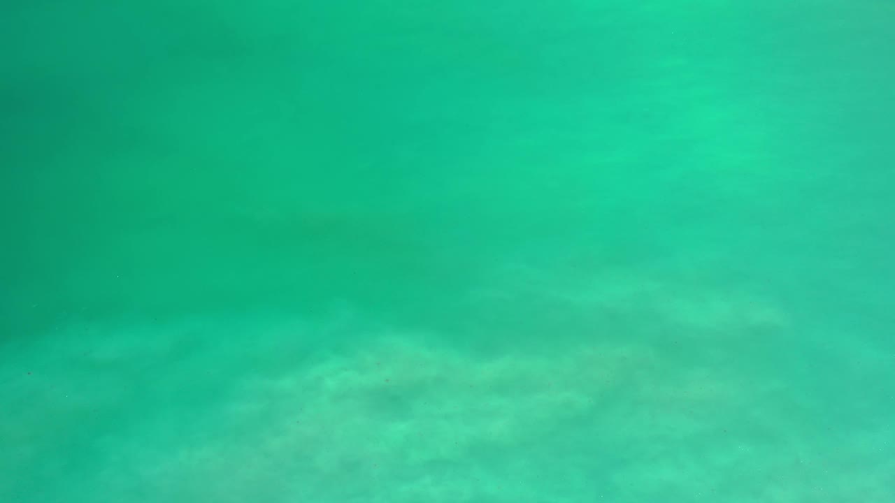 Aerial view of green-blue sea in Los Cabos, Mexico, with a pale submerged band crossing the lower part of the frame and no visible people.