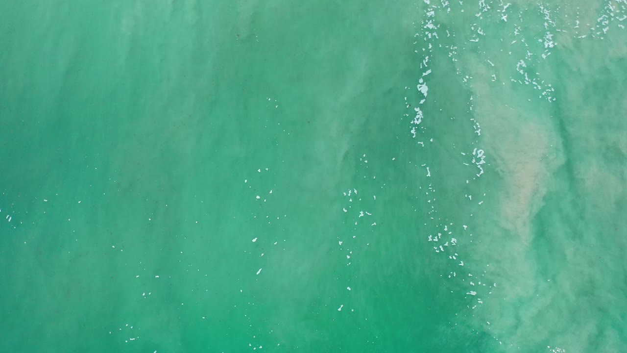 Overhead view of green ocean water in Los Cabos, Mexico, with pale underwater sand patches and no visible people.