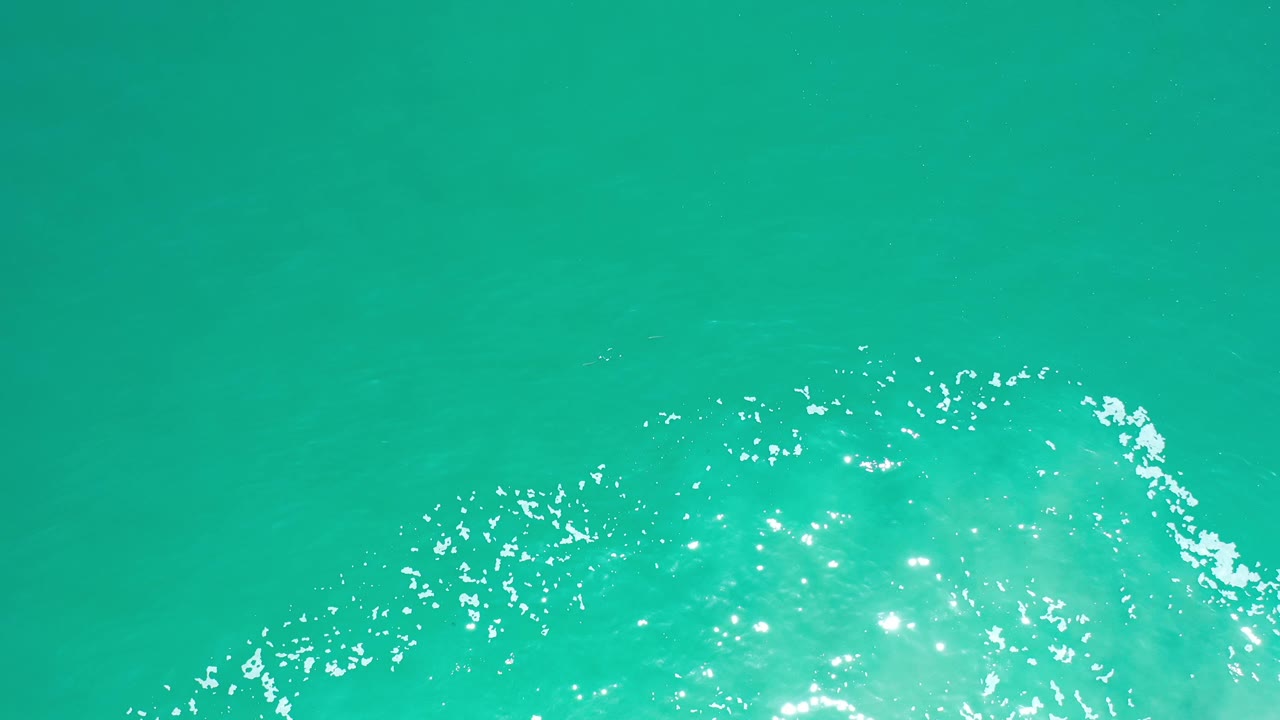 Overhead view of turquoise ocean water in Los Cabos, Mexico, with a bright patch of reflected daylight entering from the lower edge and no visible people.