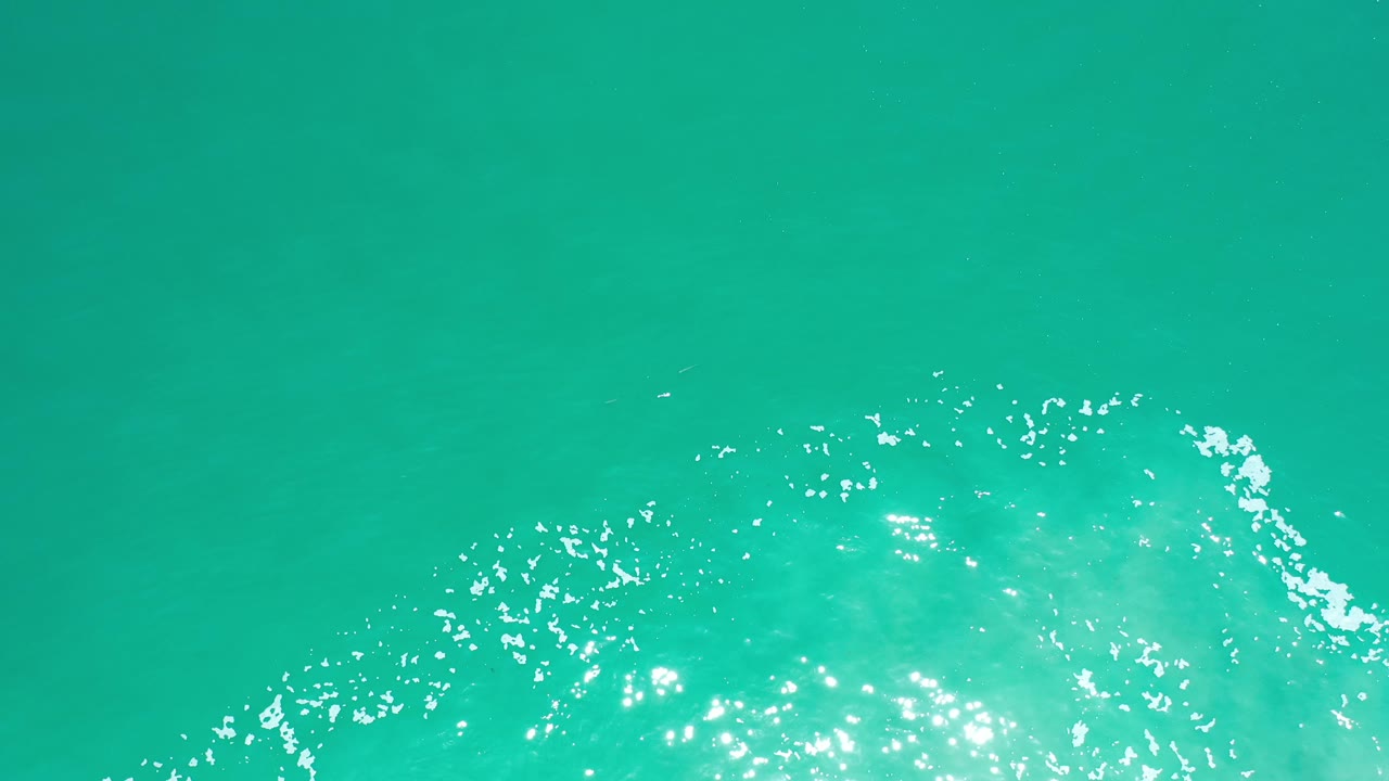 Turquoise water with sunlight sparkles and faint darker areas below the surface.