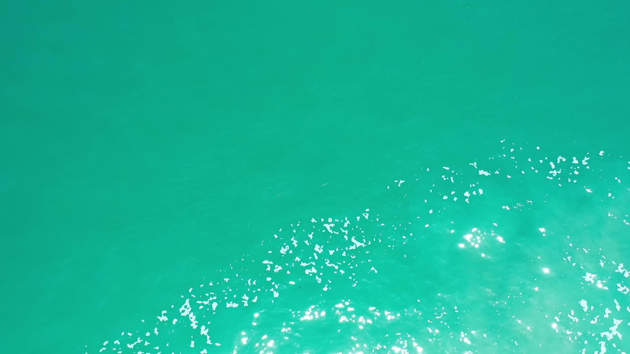 Bright green sea fills the frame in Los Cabos, Mexico, with a broad patch of rippled light lower center and no visible people.