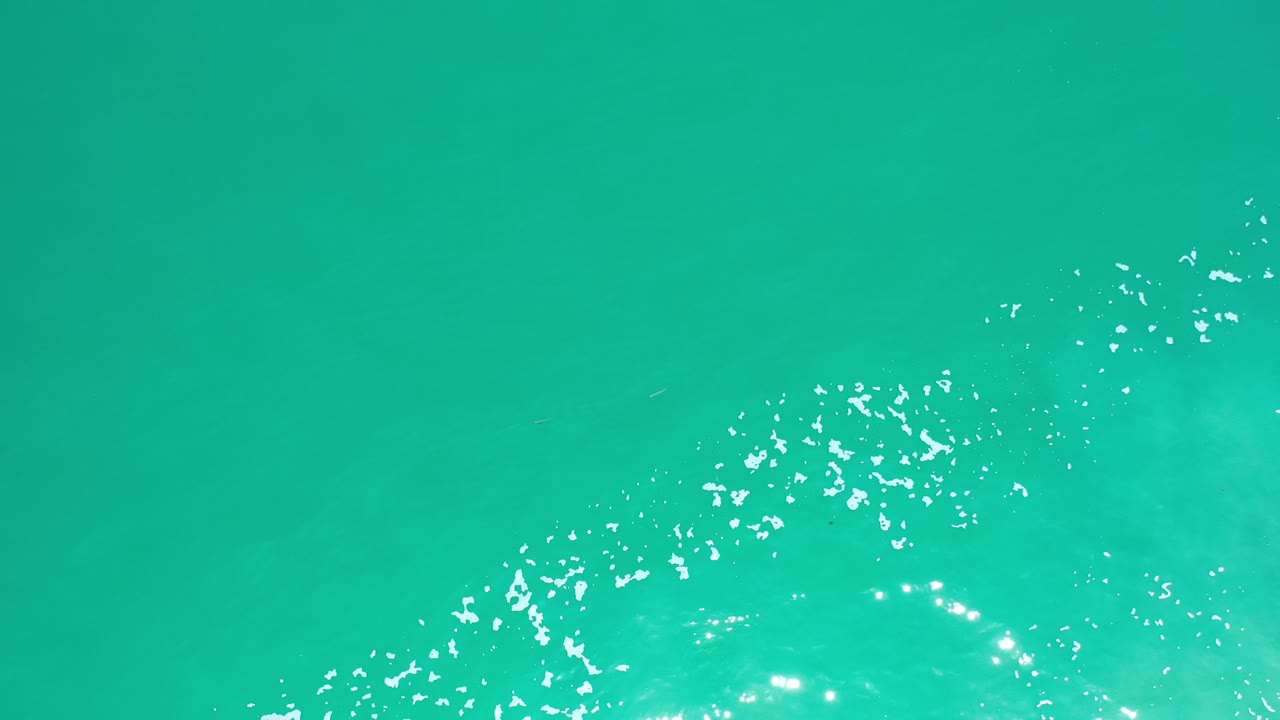 Aqua water with scattered foam and bright reflected highlights.