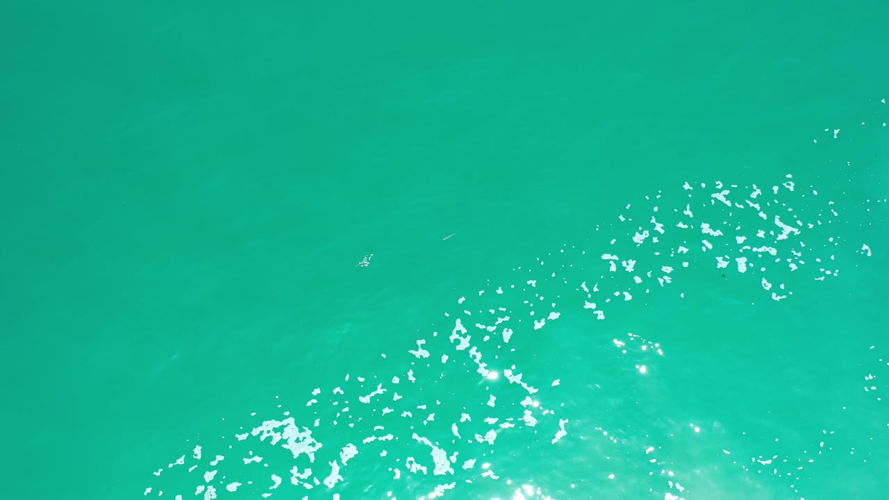 Greenish blue ocean water with sun sparkle and white foam near the lower edge.
