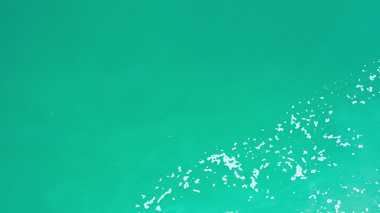 Overhead view of turquoise ocean water in Los Cabos, Mexico, with scattered white ripples crossing the lower right and no visible people.