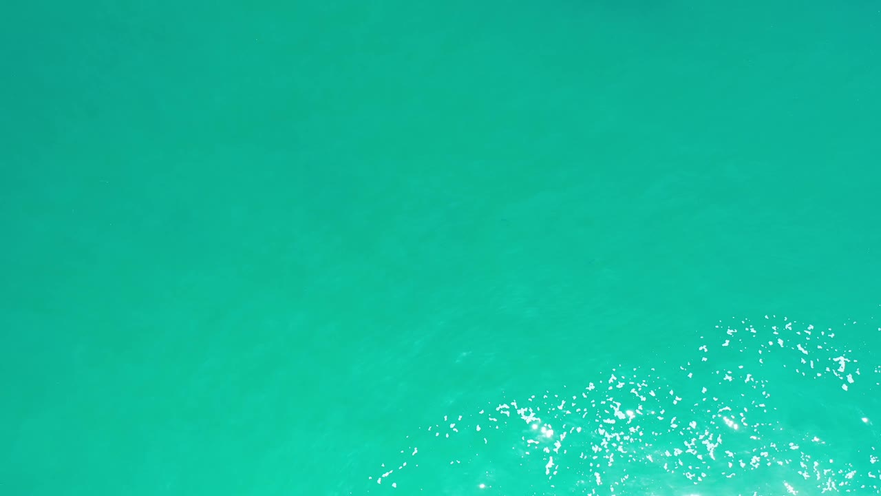 Green Los Cabos water remains tightly framed as scattered bubbles and bright reflections gather along the lower part of the image, no visible people.