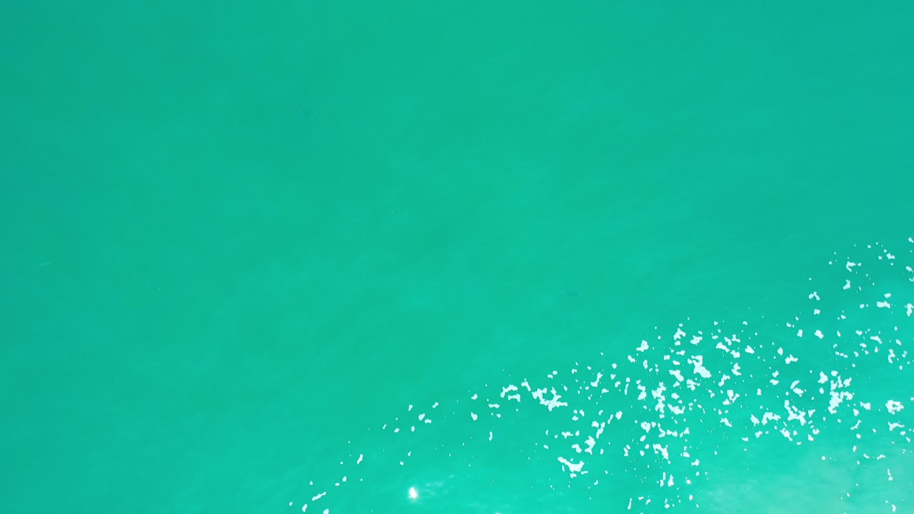 Cyan green sea water with scattered white foam flecks