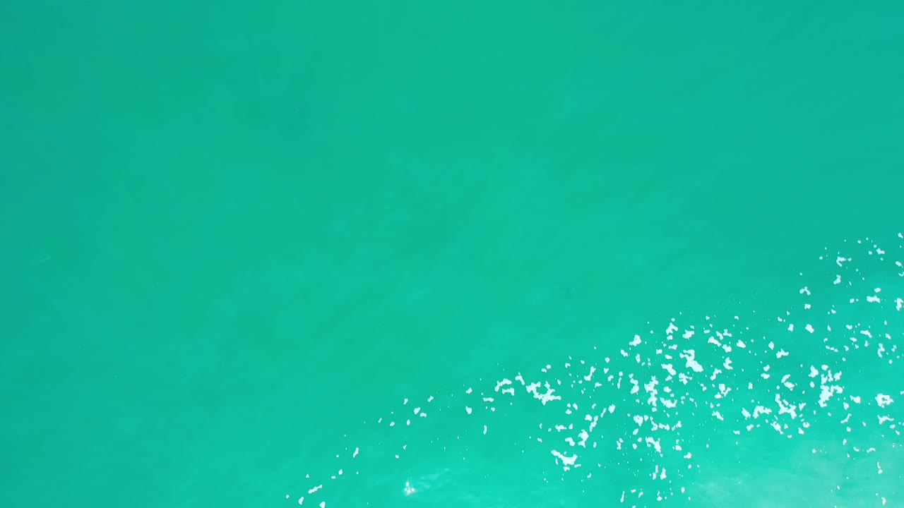 Close overhead Los Cabos sea surface with turquoise water, white foam speckles gathering across the lower center, and no visible people.