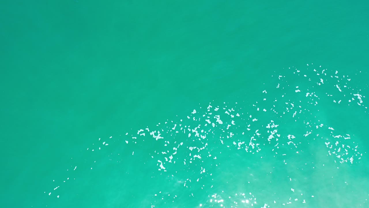 Turquoise ocean surface with bright white wave sparkle.
