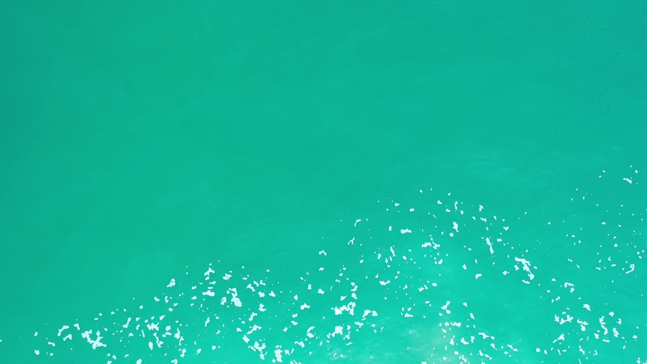Overhead Los Cabos water frame with a broad green surface, concentrated white reflections low in the image, and no visible people.