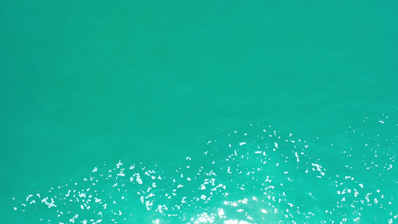 Turquoise ocean water in Los Cabos fills the frame with scattered white foam and bright sun glints near the lower edge, with no visible people.