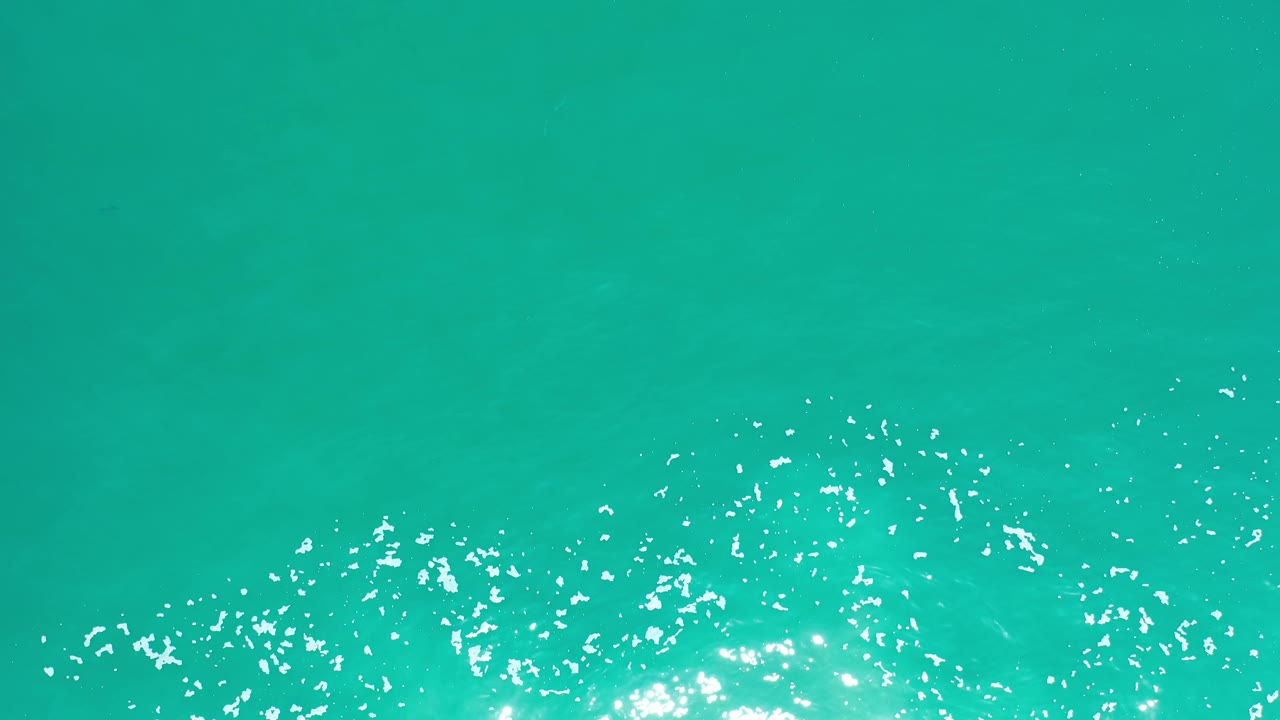 Clear teal ocean water in Los Cabos shows a band of white sparkle and foam low in the frame, with open water above and no visible people.