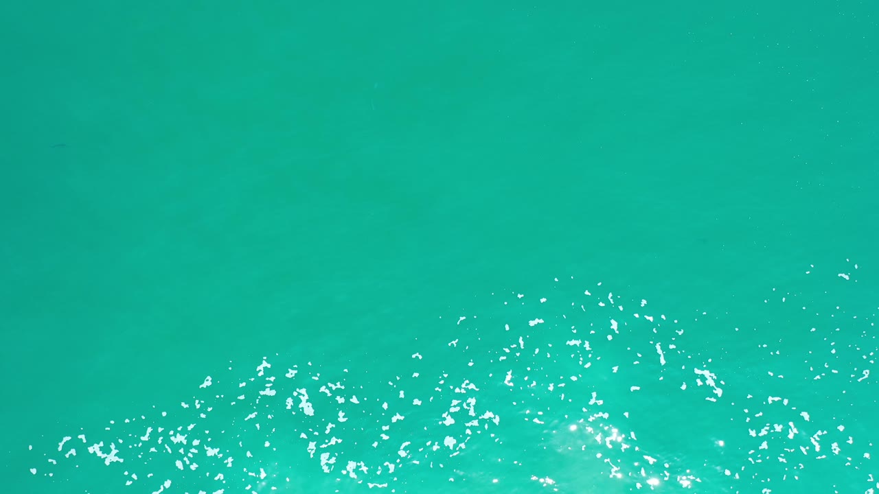 Turquoise sea surface with foam flecks crossing the lower edge