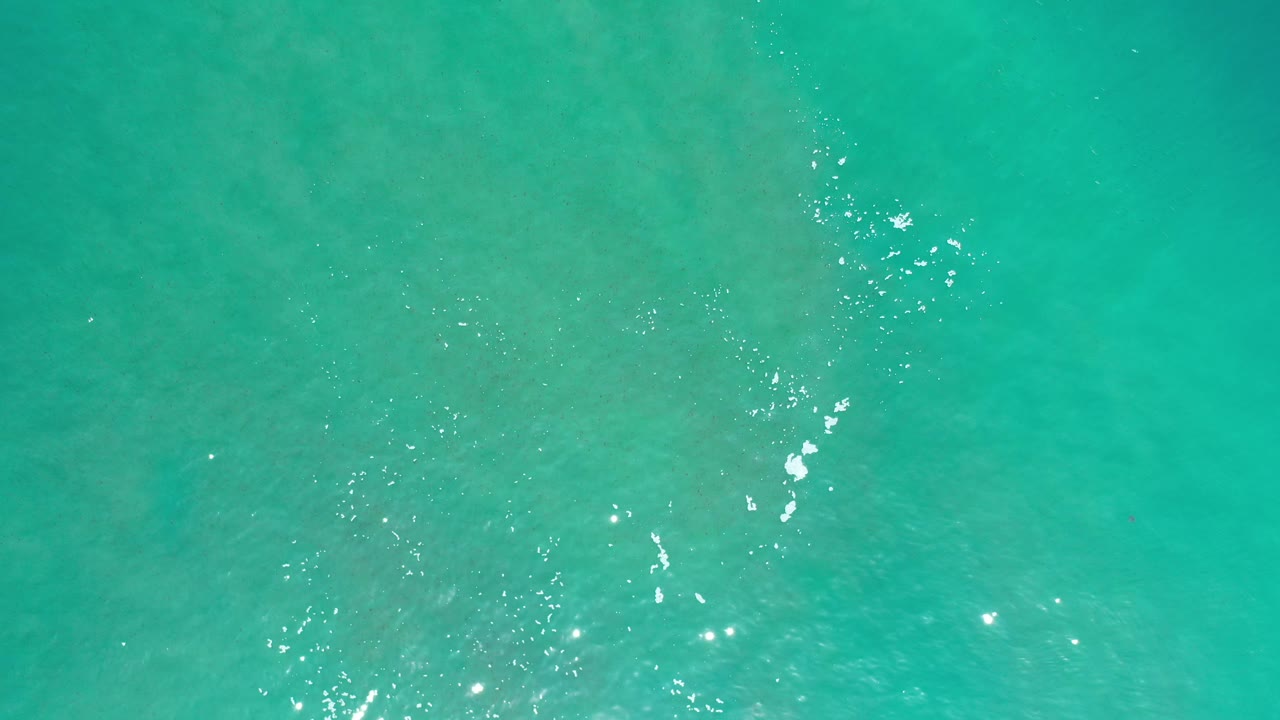 Top-down turquoise water with small bright reflections and light foam.