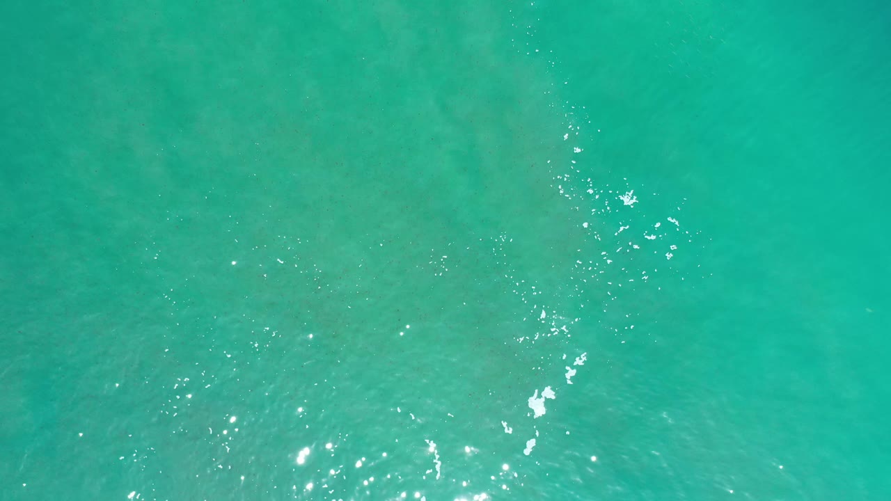Green-blue Los Cabos water fills the frame, with a loose vertical trail of bright surface glints near the center and no visible people.