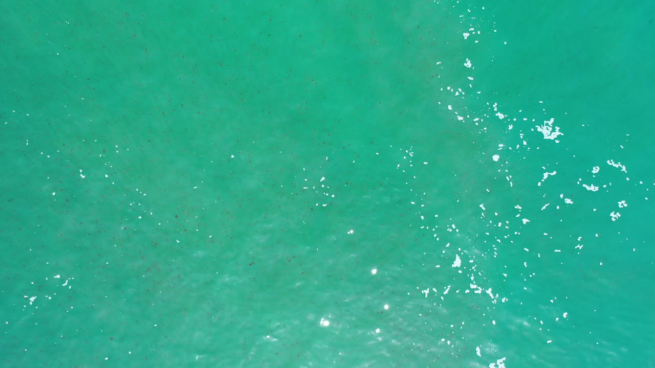 Overhead view of turquoise seawater in Los Cabos, Mexico, with scattered white sun reflections near the upper frame and no visible people.