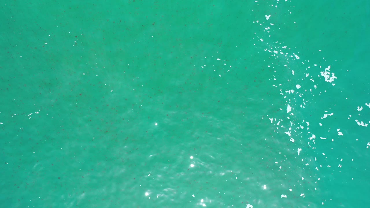 Top-down view of turquoise ocean water in Los Cabos, Mexico, with scattered white sun reflections and no visible people.